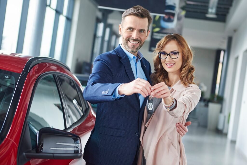 Smiling couple receiving new car keys at dealership, representing customer satisfaction and seamless auto sales with Dealer Plug